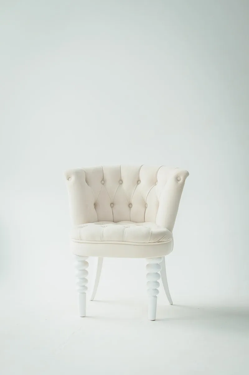 A cream tufted velvet armchair on white turned legs.