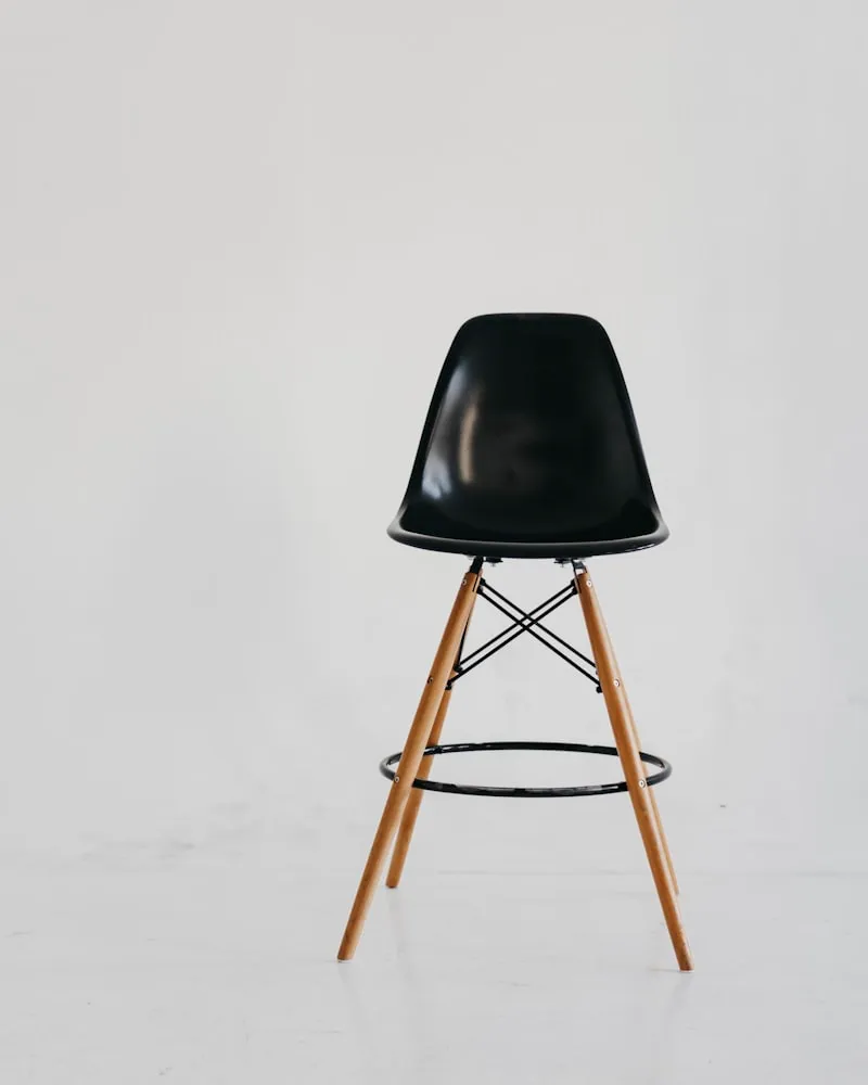 A black plastic Eames-style bar stool on light wood legs.