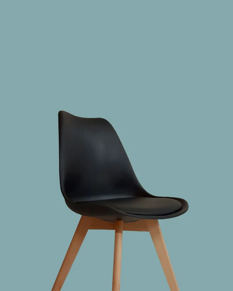 A black moulded plastic tulip chair on a teal background.