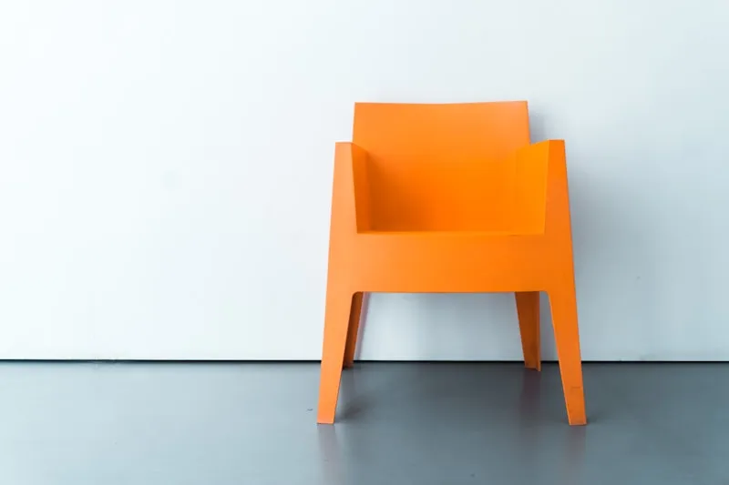 A vivid orange moulded plastic accent chair against a white wall.