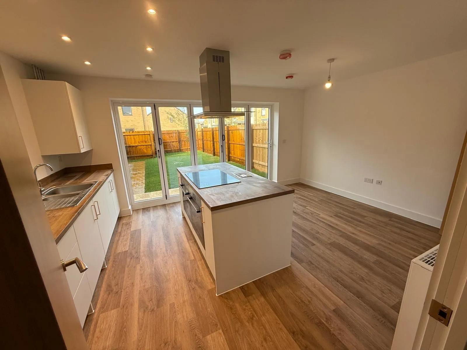 An empty new-build kitchen-diner with bi-fold doors open to the garden, no furniture, no artwork.